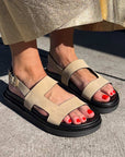 Beige sandals with black soles worn by a person on a concrete surface.