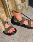 Person wearing green sandals with black soles on a concrete surface.