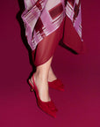 Red high-heeled shoes worn with a patterned outfit on a magenta background