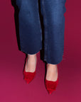 Red high-heeled shoes worn with blue jeans on a pink background