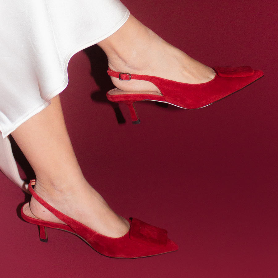 Red high-heeled shoes worn with white skirt on a red background