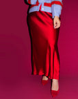 Person wearing a red satin skirt with a blue cardigan on a pink background