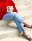 Person wearing a red sweater, blue jeans, and leopard print flats sitting on steps.