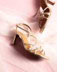 Gold high-heeled sandals on a soft pink fabric background