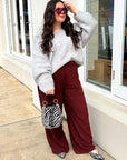 Woman wearing a gray sweater and red pants standing outside a building.