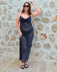 Woman in a black polka dot dress standing against a stone wall.