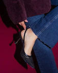 Person wearing blue jeans and black high-heeled shoes on a red background