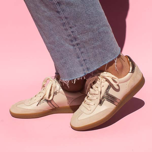 model standing in front of pink background wearing mid wash denim jeans and cream leather sneaker sneakers with gum sole
