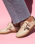 model standing in front of pink background wearing mid wash denim jeans and cream leather sneaker sneakers with gum sole