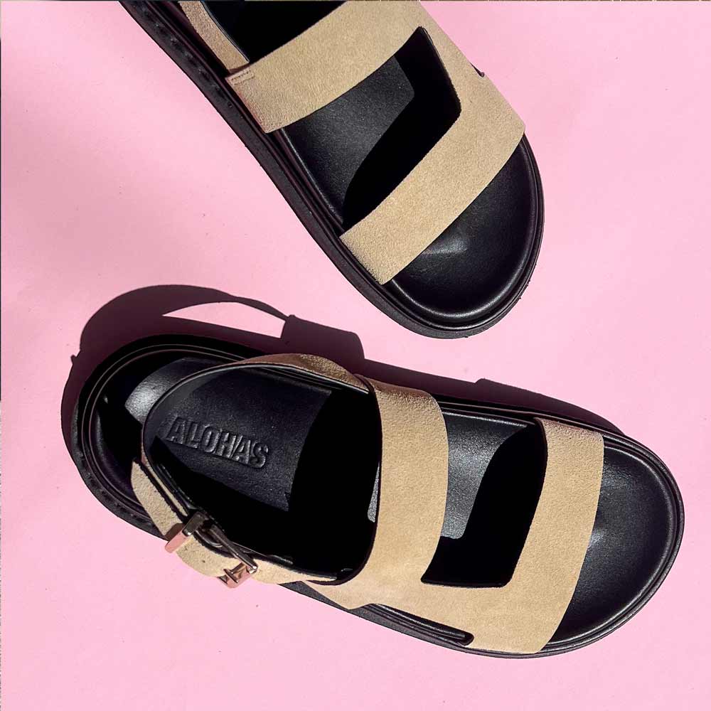 Black and beige sandals with 'Aloha' brand name on a pink background