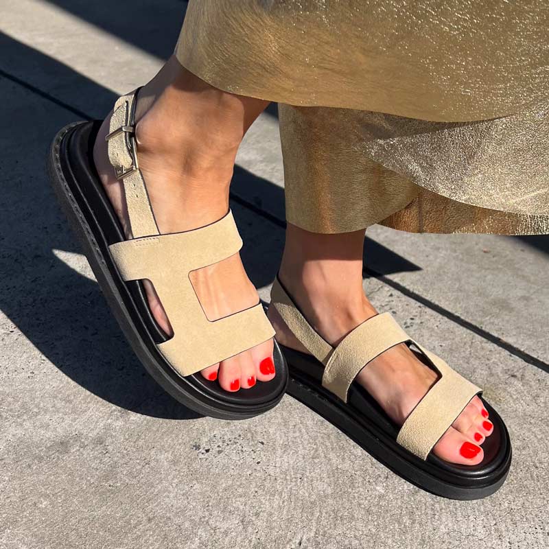 Beige sandals with black soles worn on a concrete surface