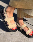 Beige sandals with black soles worn on a concrete surface
