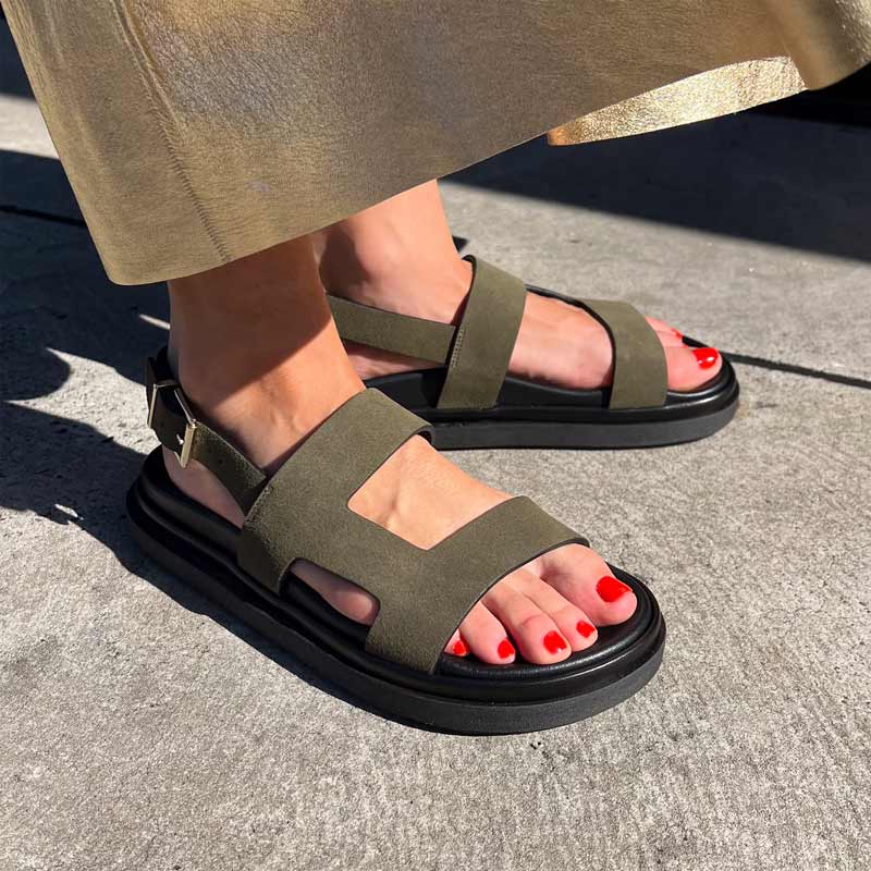 khaki sandals with black soles worn on a concrete surface
