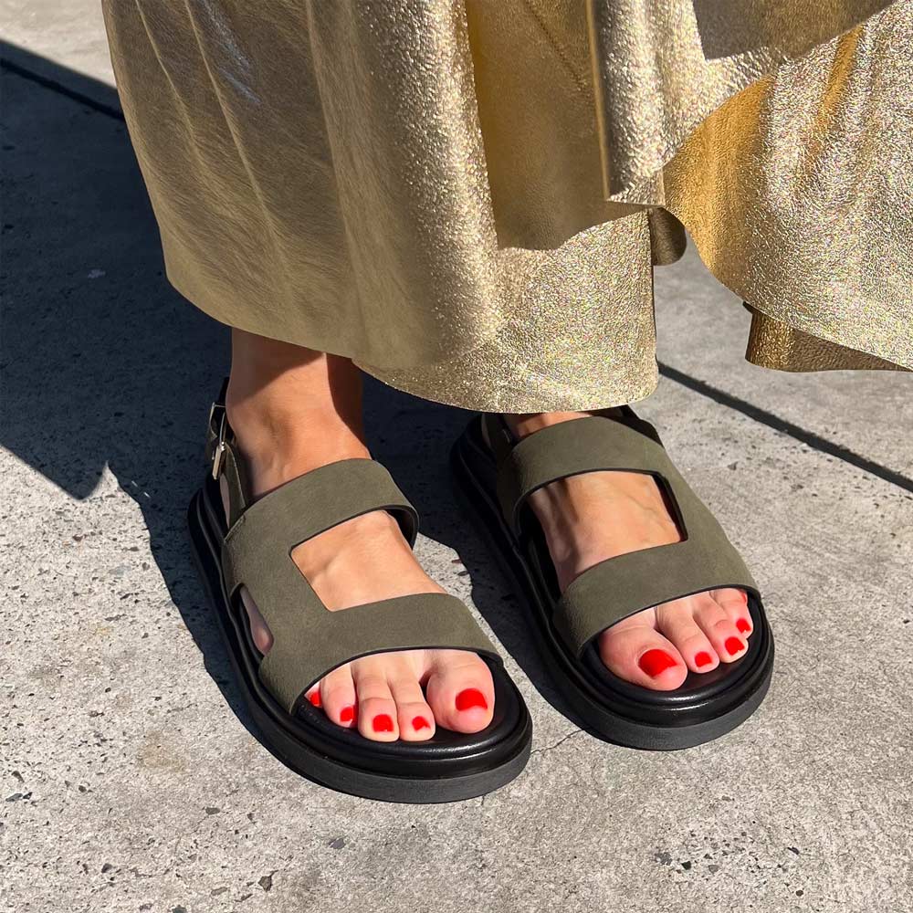 Person wearing green sandals with black soles on a concrete surface.