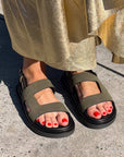 Person wearing green sandals with black soles on a concrete surface.