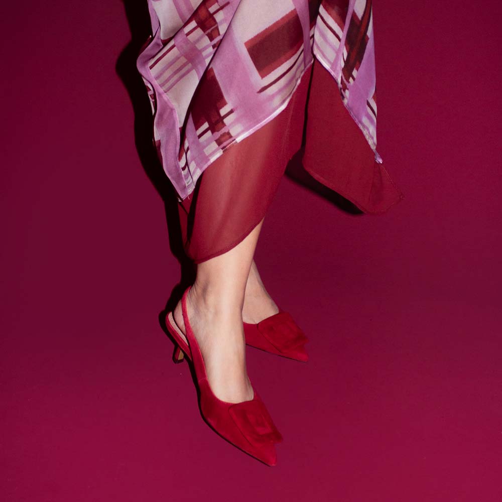 Red high-heeled shoes worn with a patterned outfit on a magenta background
