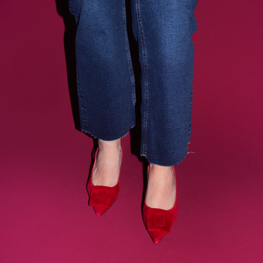 Red high-heeled shoes worn with blue jeans on a pink background