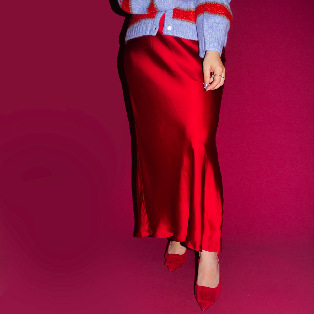 Person wearing a red satin skirt with a blue cardigan on a pink background
