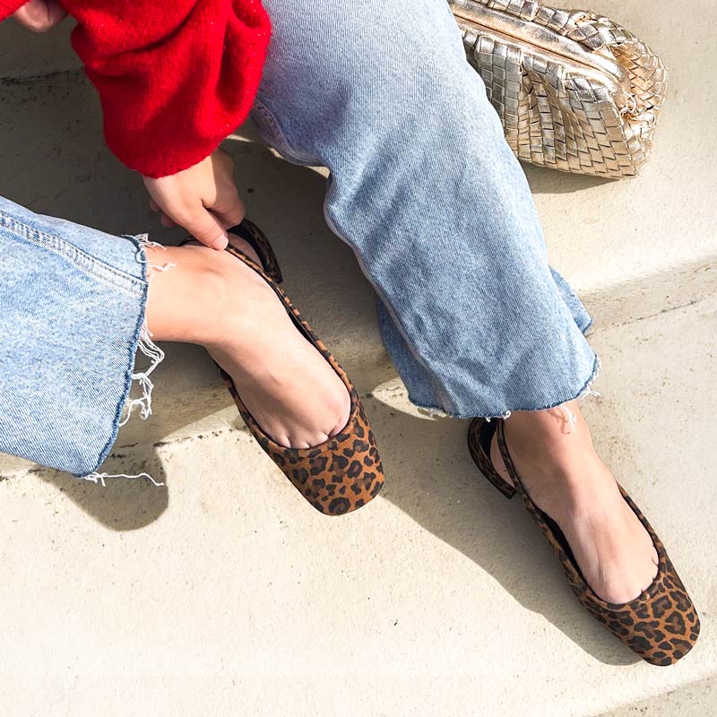 Person wearing leopard print flats with light blue jeans on a concrete surface.