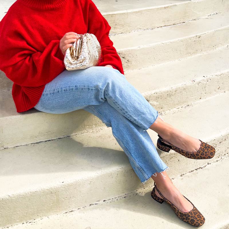 Person wearing a red sweater, blue jeans, and leopard print flats sitting on steps.