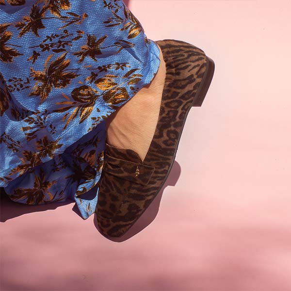 model in blue and brown printed satin pants and brown leopard print suede loafers in front of pink backdrop