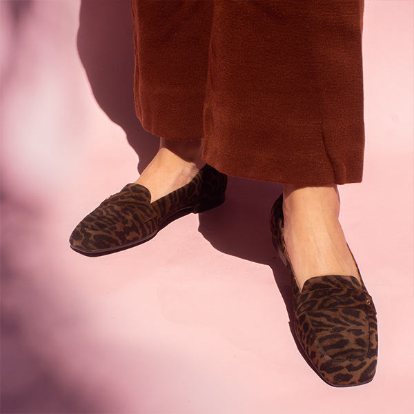 model in rust coloured pants and brown leopard print suede loafers in front of pink backdrop