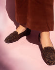 model in rust coloured pants and brown leopard print suede loafers in front of pink backdrop