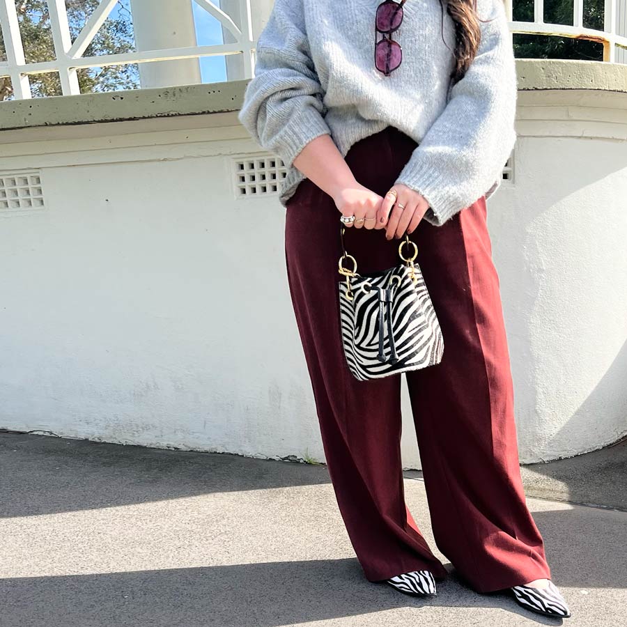 Person wearing a light gray sweater and burgundy pants, holding a zebra-striped handbag.