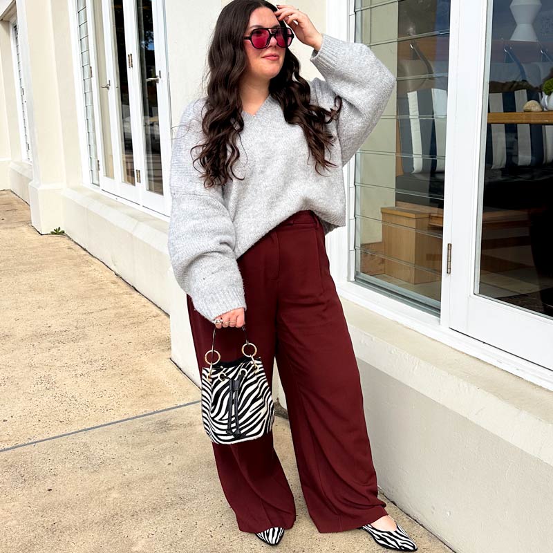 Woman wearing a gray sweater and red pants standing outside a building.
