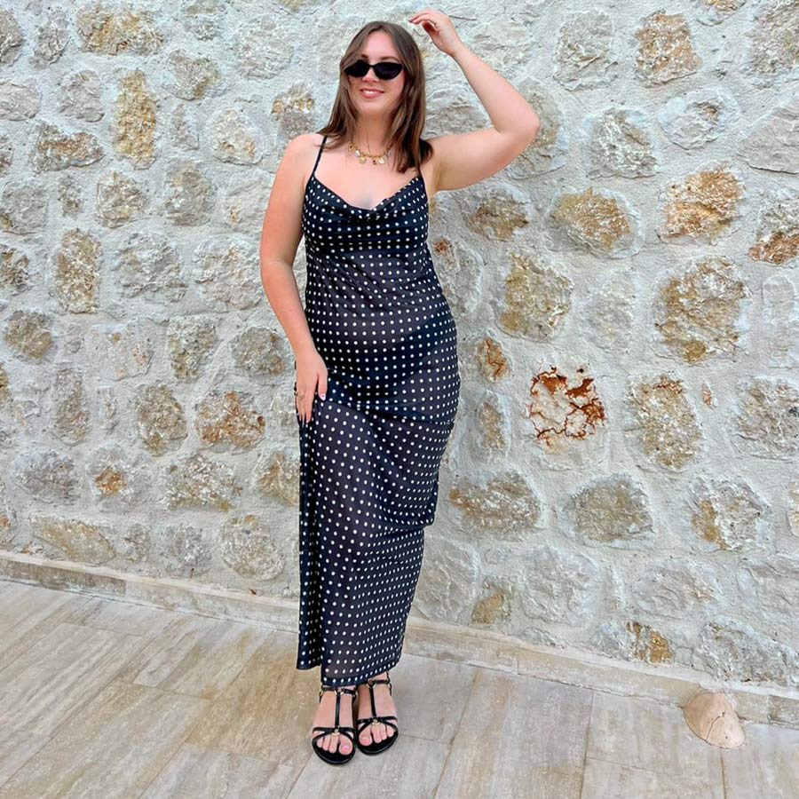 Woman in a black polka dot dress standing against a stone wall.