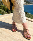 Person wearing a white lace dress and straw hat with a scenic background of water and greenery.