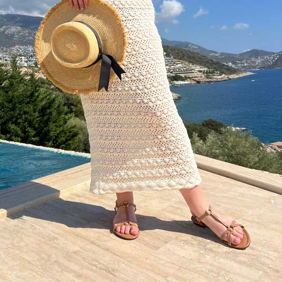 Person holding a straw hat with a scenic view of a coastal landscape.