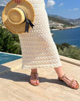 Person holding a straw hat with a scenic view of a coastal landscape.