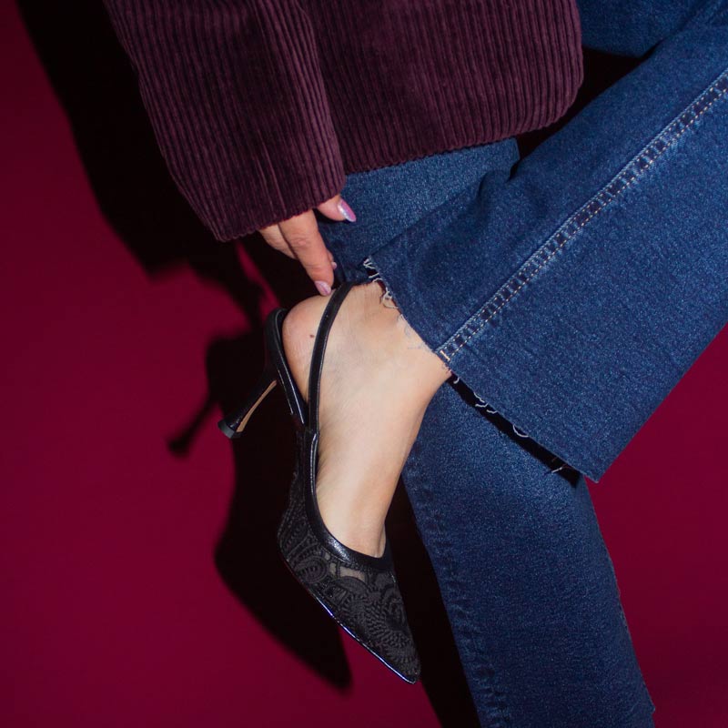 Person wearing blue jeans and black high-heeled shoes on a red background