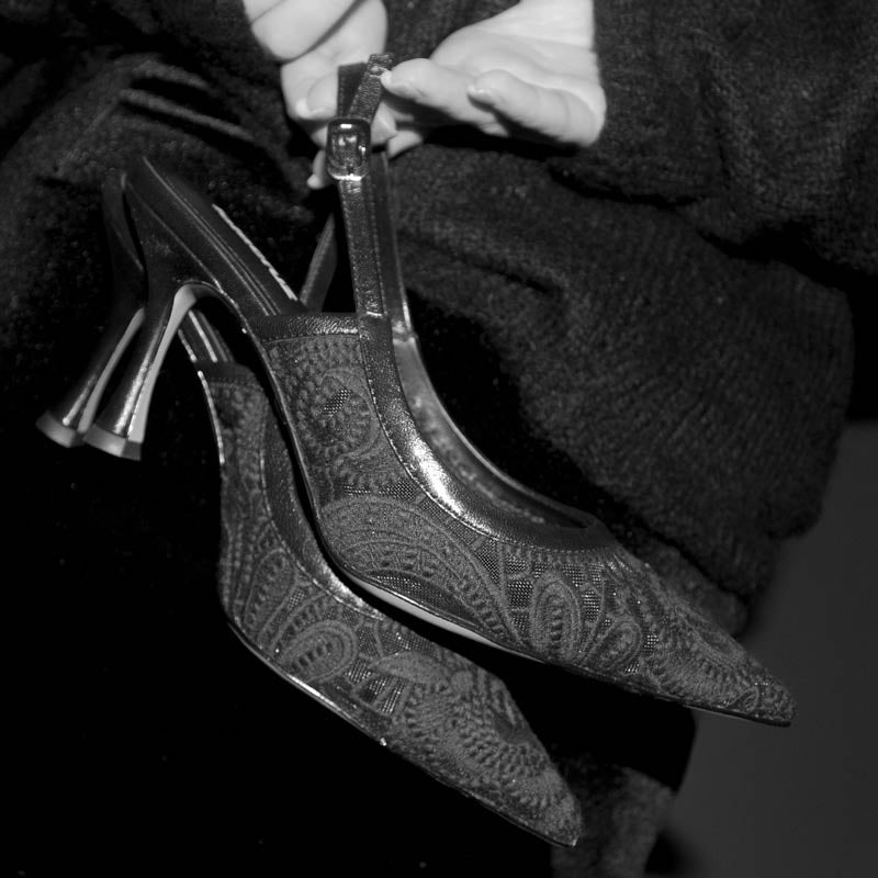 Black high-heeled shoes with intricate design held by a person against a dark background