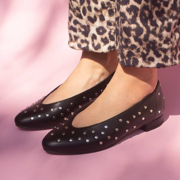 model in cropped leopard print jeans and black leather ballet flats with silver studs in front of pink backdrop