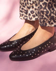 model in cropped leopard print jeans and black leather ballet flats with silver studs in front of pink backdrop