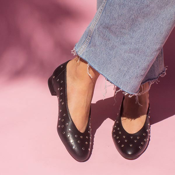 model in mid wash jeans and black leather ballet flats with silver studs in front of pink backdrop