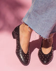 model in mid wash jeans and black leather ballet flats with silver studs in front of pink backdrop