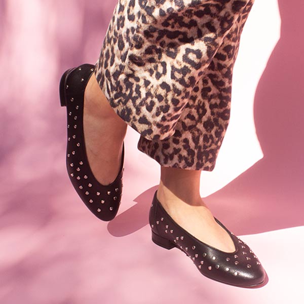 model in cropped leopard print jeans and black leather ballet flats with silver studs in front of pink backdrop