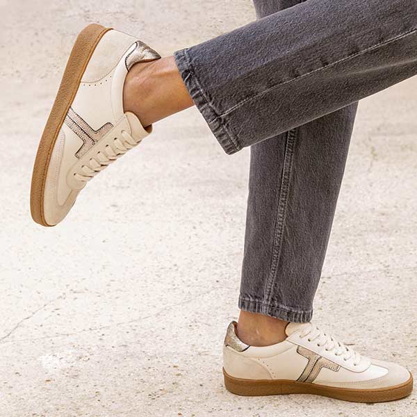 model standing on the street in pair of grey wash jeans and cream leather sneakers with gum sole.