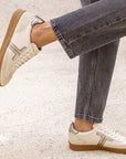 model standing on the street in pair of grey wash jeans and cream leather sneakers with gum sole.