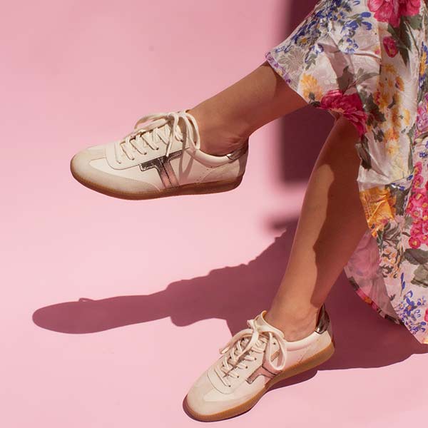 model sitting crossed legged on chair wearing floral print skirt and cream leather sneaker sneakers with gum sole in front of pink background