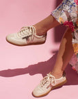 model sitting crossed legged on chair wearing floral print skirt and cream leather sneaker sneakers with gum sole in front of pink background