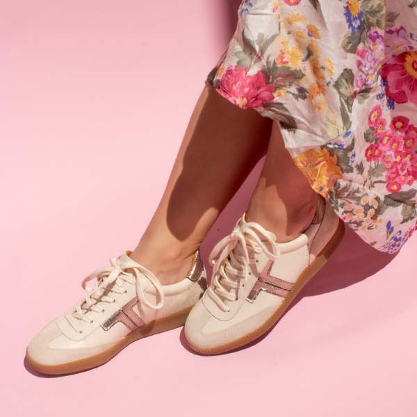 model sitting crossed legged on chair wearing floral print skirt and cream leather sneaker sneakers with gum sole in front of pink background