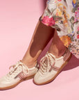 model sitting crossed legged on chair wearing floral print skirt and cream leather sneaker sneakers with gum sole in front of pink background