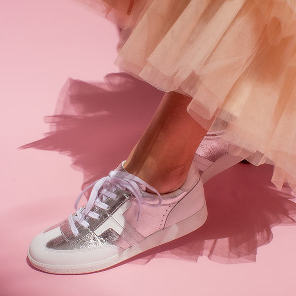 model wearing peach tulle skirt and silver leather sneaker sneakers in front of pink background