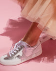 model wearing peach tulle skirt and silver leather sneaker sneakers in front of pink background