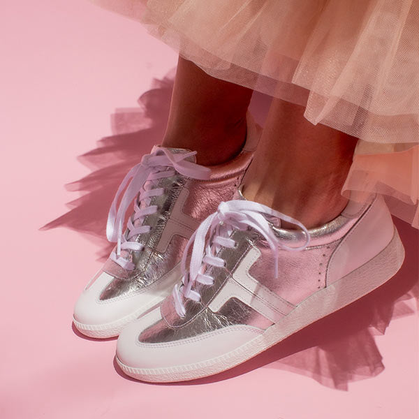 model wearing peach tulle skirt and silver leather sneaker sneakers in front of pink background