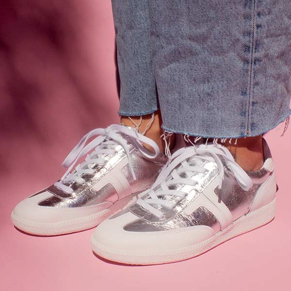 model wearing light wash denim jeans  and silver leather sneaker sneakers in front of pink background